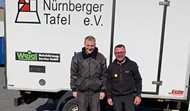 Zwei Personen stehen vor einem weißen Lieferwagen mit dem Logo 'Nürnberger Tafel e.V.' und weiteren Aufklebern. Die Personen tragen schwarze Jacken.