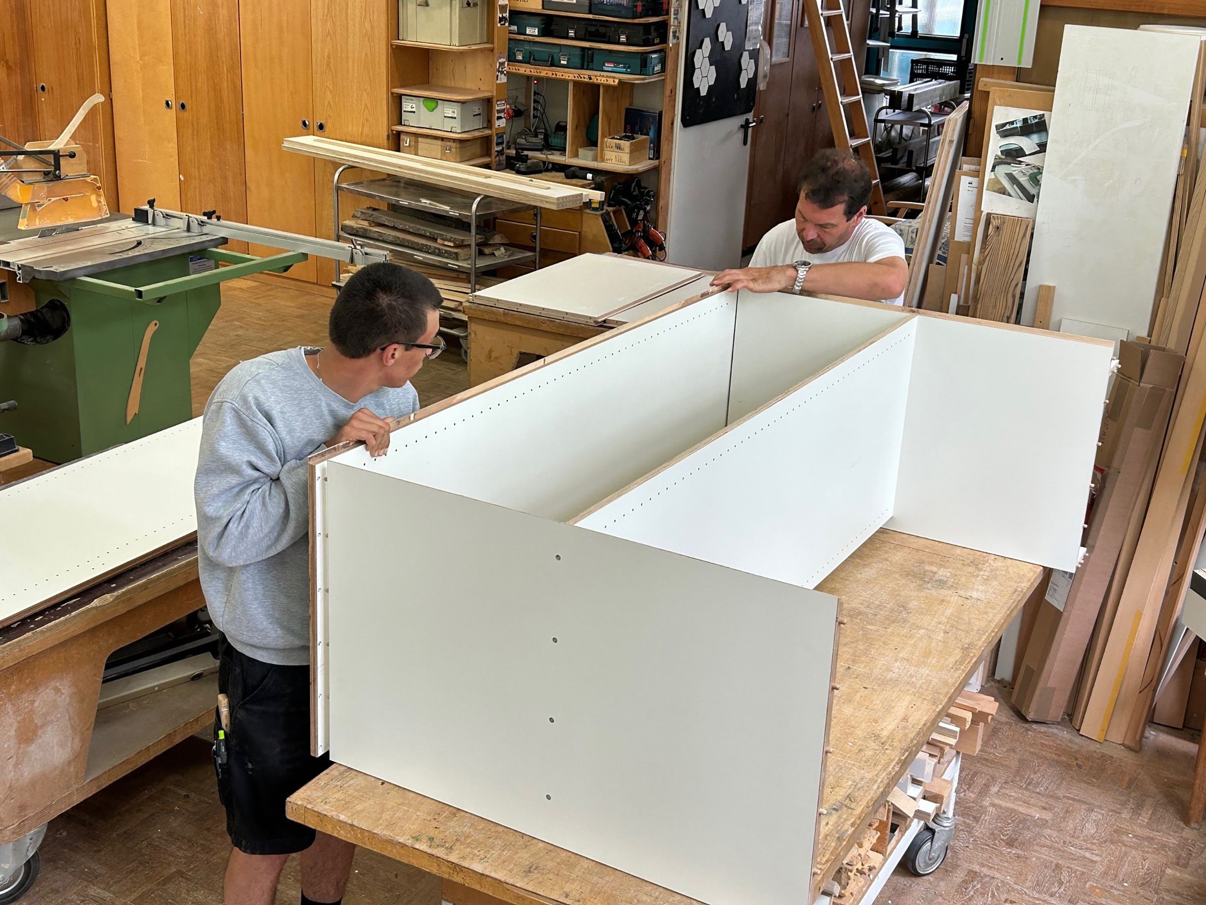 Zwei junge Männer mit bauen in einer Schreinerei ein Holzregal zusammen