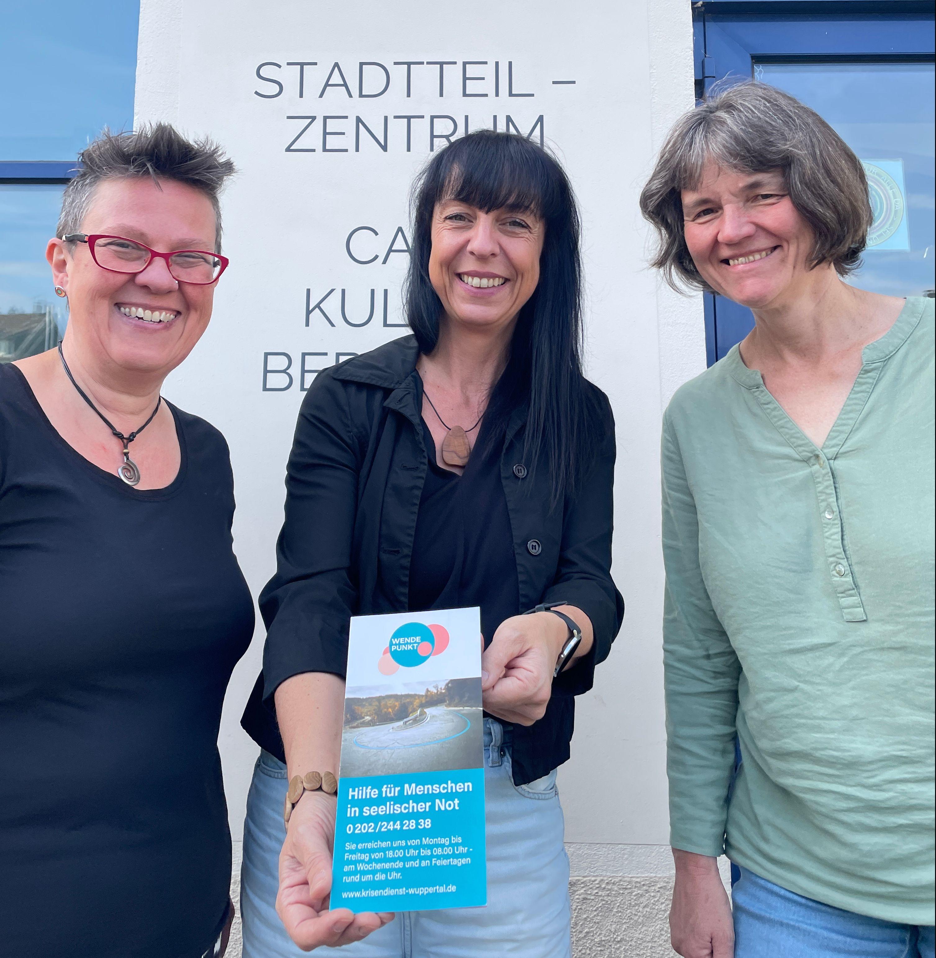 Drei strahlende Frauen präsentieren einen Flyer