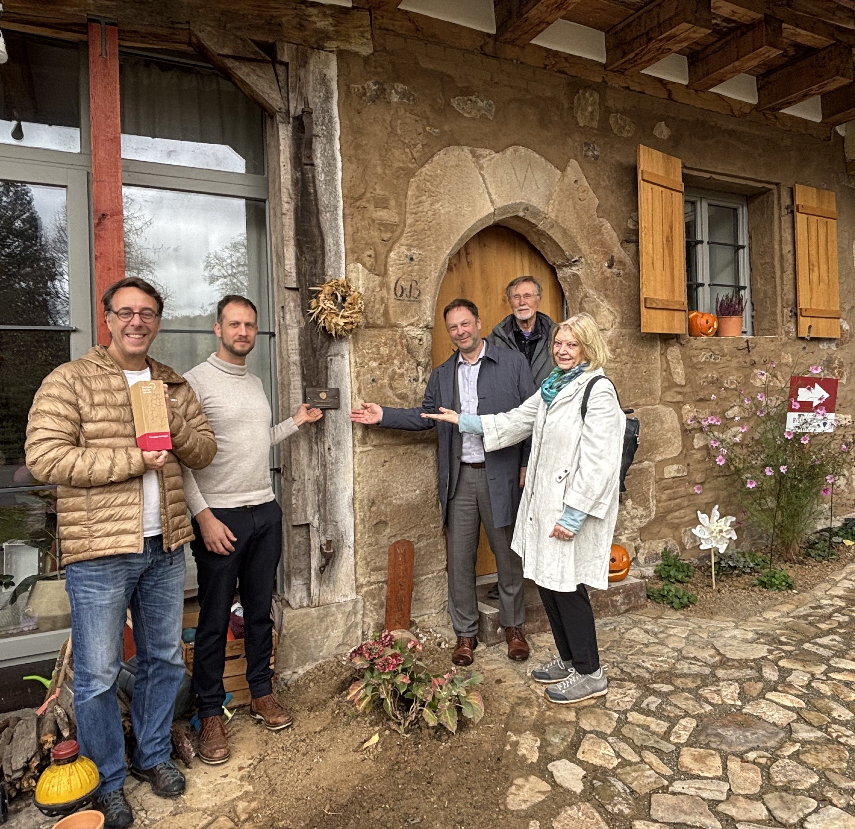 Eine Gruppe Menschen mit einer Bronzetafel vor einer Scheune